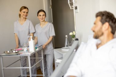 İki genç hemşire, koğuşta hasta ziyaretine gelen ilaç arabalarını itiyor. Hemşirelik ve tıbbi destek kavramı