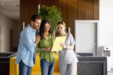 Hemşire, modern bir kliniğin bekleme odasında doktor randevusundan önce bir kadın ve bir erkek ile iletişim kuruyor. Sağlık hizmeti, destek ve bakım konsepti