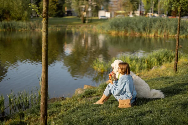Молодая Женщина Ест Мороженое Сидя Своей Милой Белой Собакой Озера — стоковое фото