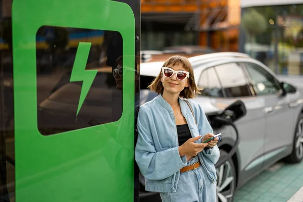 Ung Kvinne Står Med Smarttelefon Venter Hennes Elektriske Bil Skal – stockfoto
