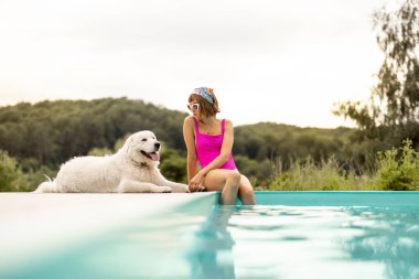 Kadın tatlı köpeğiyle havuz kenarında dinleniyor, yaz tatilini birlikte geçiriyor. Evcil hayvanlarla arkadaşlık ve yaz tatili kavramı