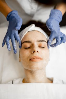 Güzellik salonundaki güzellik prosedüründen önce yüzüne krem süren genç bir kadın, yukarıdan yakından görülüyor.