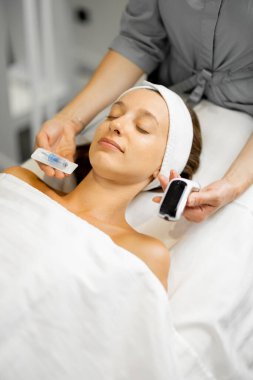 Kozmetik uzmanı cilt bakımıyla ilgili bir güzellik ameliyatından önce genç bir kadın, hastalarının yüzüne yakın iğneyle dermapen tutuyor.