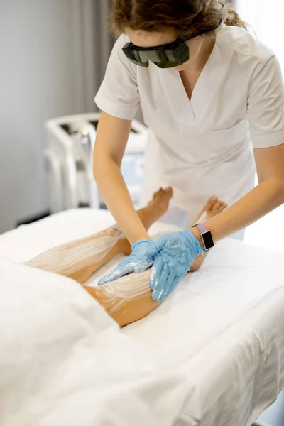 Young worker of a beauty salon during hair removal procedure on a womans legs. Depilation concept and beauty procedures