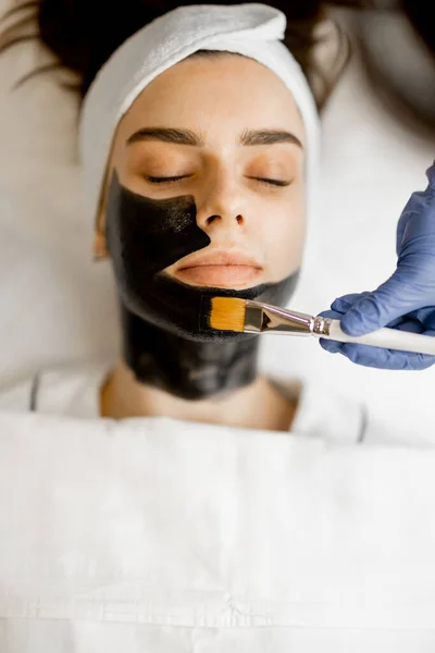 Applying carbon mask with a brush to a womans face, preparing for a laser carbon peeling in beauty salon, close-up. Face care concept and beauty procedures