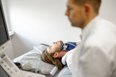 Şah damarının ultrason teşhisi sırasında genç bir adam. Ultrason teşhisi ve erkek sağlığı kavramı. Kardiyovasküler hastalıkların incelenmesi fikri