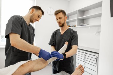 Travma bölümündeki hastalara bandaj yapan iki doktor. Yaralanmalardan sonra travma, ortopedi ve rehabilitasyon kavramı