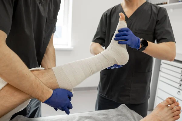 2人の医療従事者が外傷部の患者脚に包帯を作っている 傷害後の外傷 整形外科 リハビリの概念 — ストック写真