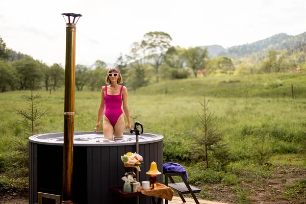 若い女性が熱い風呂に薪で加熱し 山の中で休んで入浴 自然の中でのレクリエーションやスパの手順の概念 — ストック写真