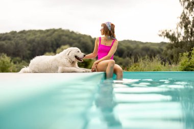 Kadın tatlı köpeğiyle havuz kenarında dinleniyor, yaz tatilini birlikte geçiriyor. Evcil hayvanlarla arkadaşlık ve yaz tatili kavramı