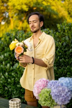 Man arranges a bouquet with cut flowers in garden. Male florist works in his garden outdoors