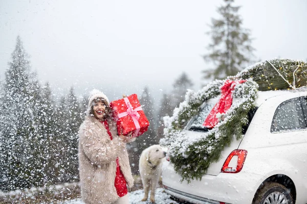 一个快乐女人的画像站在暴风雪中的礼品盒旁 乘坐着装饰着圣诞花环和圣诞树的汽车 寒假快乐与魔法的概念 — 图库照片