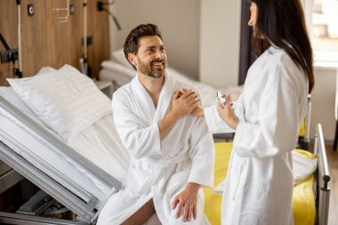 Tıbbi koğuşta tedavi gören erkek ve kadın, ameliyattan sonra kocasına destek oluyor, rahat bir medikal süitte dinleniyor.