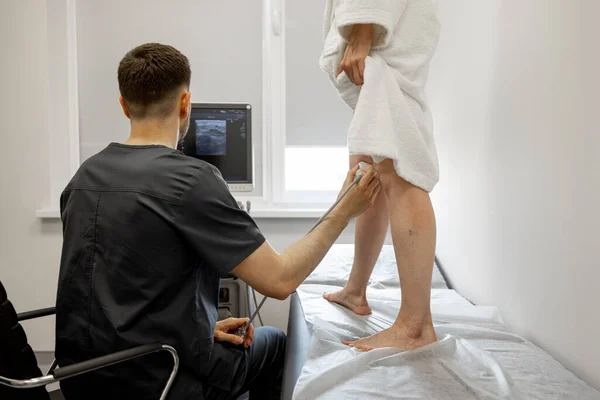 Ultrasound specialist is scanning the veins on a womans leg, examining veins for varicose treatment