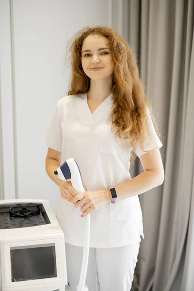 Portrait of a young worker of beauty salon standing near laser epilation machine