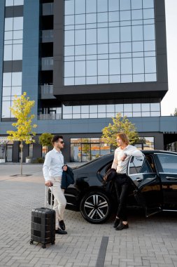 Siyah bavullu iş adamları, gün batımında ofis binasında ya da otelde duran premium arabalarıyla seyahat ediyorlar. İş gezileri ve ulaşım kavramı