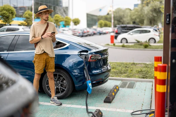 Mies Odottaa Että Hänen Autonsa Ladataan Kun Hän Seisoo Puhelimen — kuvapankkivalokuva