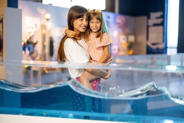 Mom with little daughter learn physics interactively on a model that shows physical phenomena while visiting a science museum. Concept of childrens entertainment and learning