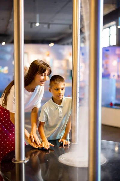 Mom with a little boy learn physics interactively on a model that shows physical phenomena while visiting a science museum. Concept of childrens entertainment and learning