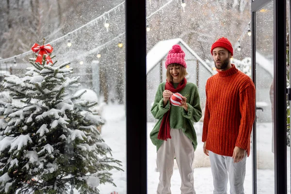 男人和女人准备用喜庆的球装饰圣诞树 快乐地站在雪地的后院 在家中庆祝寒假的年轻家庭 — 图库照片
