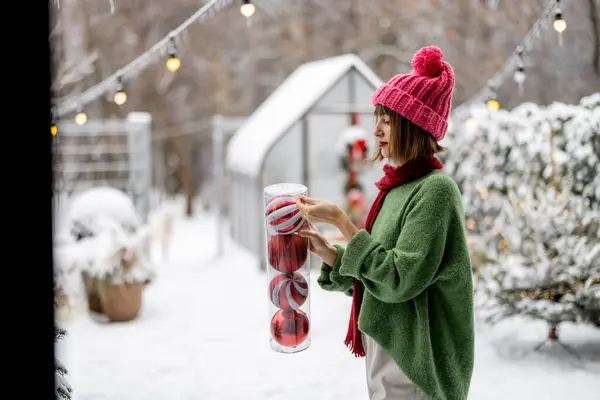 Молода Жінка Прикрашає Різдвяну Ялинку Святковими Кульками Стоячи Терасі Засніженому — стокове фото