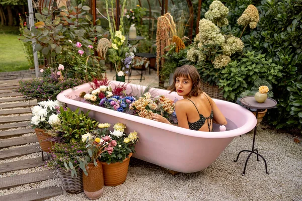 Wanita Berbaring Bak Mandi Merah Muda Dengan Banyak Bunga Taman — Stok Foto