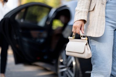 İş kadını arabadan çıkıyor, el çantası taşıyor, çantanın üstüne yakın çekim yapıyor. İş hayatı ve kadın tarzı kavramı