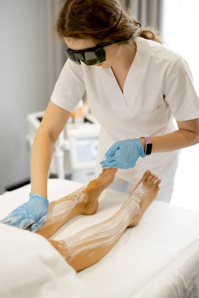Young worker of a beauty salon during hair removal procedure on a womans legs. Depilation concept and beauty procedures