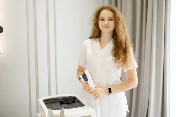 Portrait of a young worker of beauty salon standing near laser epilation machine