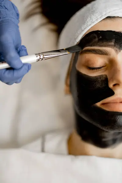 Applying carbon mask with a brush to a womans face, preparing for a laser carbon peeling in beauty salon, close-up. Face care concept and beauty procedures
