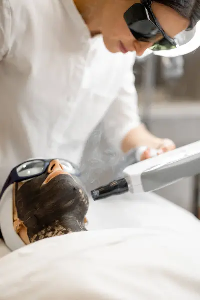 Cosmetologist makes laser carbon peeling on womans face at beauty salon. Concept of beauty facial treatments