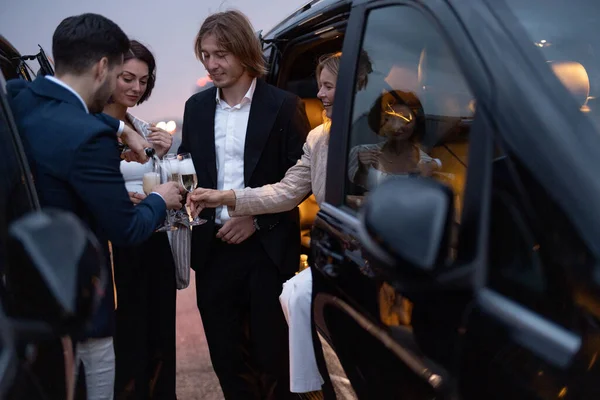 Group of business partners have fun together, drinking alcohol while celebrating between cars on parking lot at night