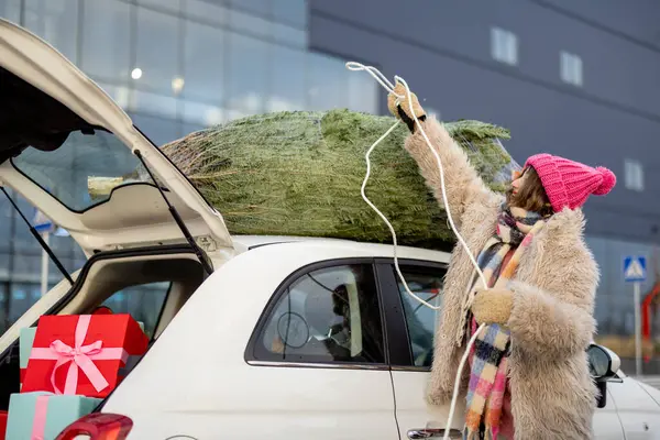 在购物中心购物的时候 一位年轻的女士用绳子把圣诞树绑在她的车顶上 寒假和购物的概念 — 图库照片