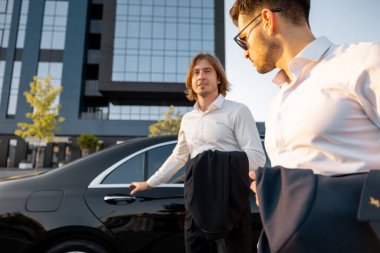 İki işadamı gün batımında otel ya da ofis binasının yakınında lüks bir arabaya binip işten sonra araba kullanacaklar. Ulaşım ve iş yaşam tarzı kavramı