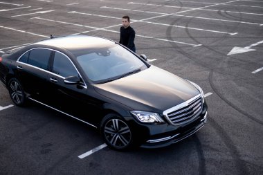 Park yerindeki lüks lüks bir arabanın yanında şoför, yukarıdan manzaralı.