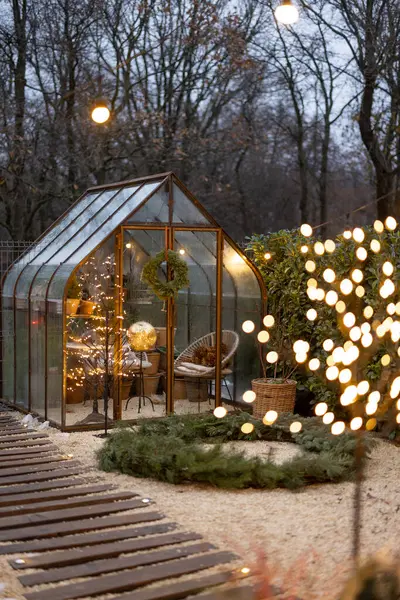 Beautiful backyard with vintage glasshouse and Christmas wreath decorated with garlands during winter time. Concept of coziness and decoration on winter holidays