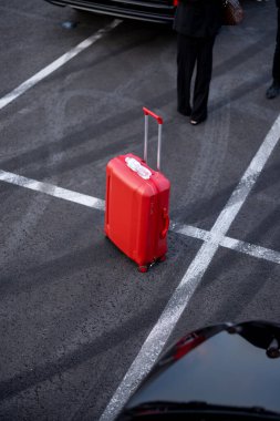 Dışarıdaki otoparkın asfaltında kırmızı bavul, iş seyahati kavramı.