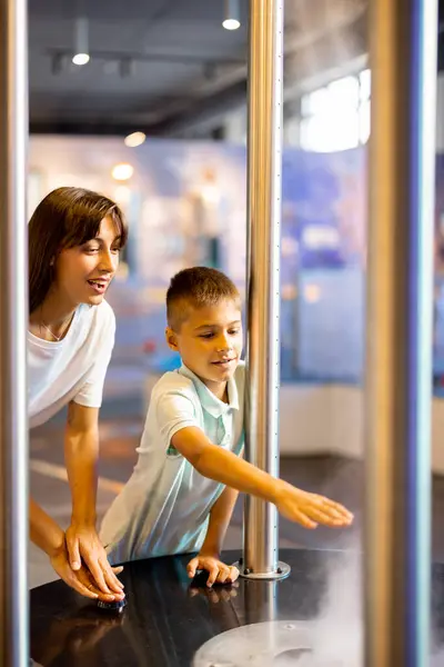 妈妈和一个小男孩在参观科学博物馆时 在一个展示物理现象的模型上互动地学习物理 儿童娱乐和学习的概念 — 图库照片