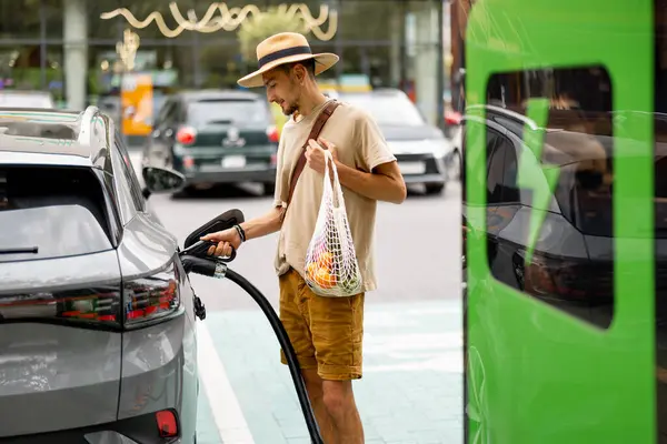 Mannen Med Dagligvarer Som Venter Elektrisk Bil Som Skal Belastes – stockfoto