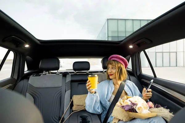 Nuori Tyylikäs Nainen Käyttää Älypuhelinta Istuessaan Kahvikupin Kukkakimpun Kanssa Auton — kuvapankkivalokuva