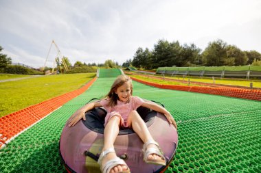 Mutlu küçük kız yaz pistinde şişme kızak tüpüne atlayıp lunaparkta eğleniyor. Yaz tatili ve çocuk eğlencesi kavramı