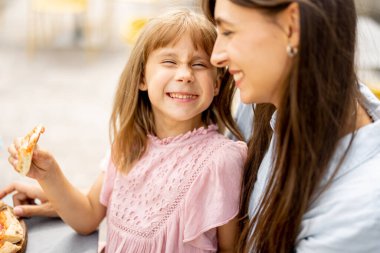 Küçük kızıyla birlikte neşeli bir anne dışarıda pizza yiyor, yaz tatilinde lunaparka gidiyor.