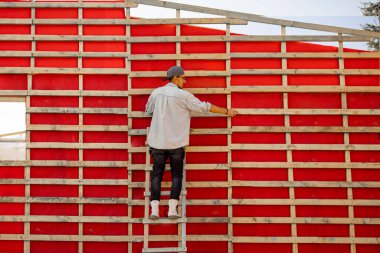 Tamamlanmamış ahşap çerçeve inşaatındaki bir adamın portresi ya da marangoz. Tamirci ev inşa ediyor.