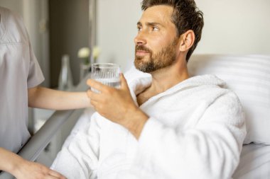Yetişkin bir hasta tıbbi serviste dinlenirken su içiyor. Klinikteki rehabilitasyon sırasında tıbbi destek ve yardım