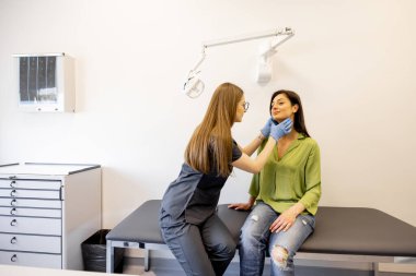 Genç doktor dermatolog ya da kozmetikçi kadın hastaların yüz derilerini muayene ediyor.