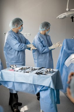 Üniformalı iki cerrah ameliyathanede bir hastayı ameliyat etmeye hazır bekliyor. Cerrahi tedavi ve invazif prosedür konseptine hazırlık