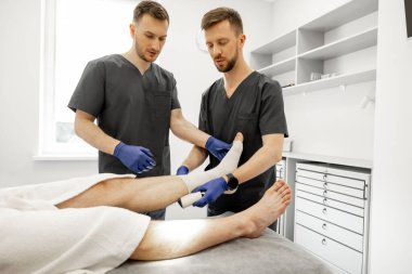 Travma bölümündeki hastalara bandaj yapan iki doktor. Yaralanmalardan sonra travma, ortopedi ve rehabilitasyon kavramı