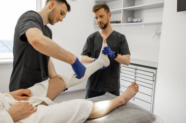 Travma bölümündeki hastalara bandaj yapan iki doktor. Yaralanmalardan sonra travma, ortopedi ve rehabilitasyon kavramı