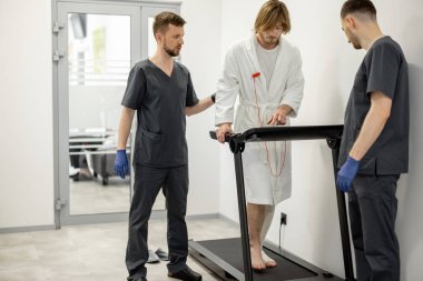 Rehabilitasyon sırasında iki rehabilitasyon uzmanı bir hastanın koşu bandında yürümesine yardım ediyor. Travma tedavisi ve tıbbi destek kavramı