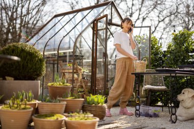 Genç bir kadın bahçede ya da küçük bir dükkanda çiçeklerle ilgilenirken telefonla konuşuyor. Çiçek yetiştirme işi kavramı